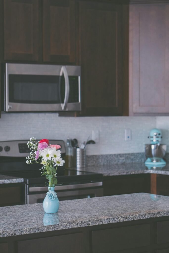 pexels-photo-1103560-1103560 Stylish kitchen interior featuring granite countertops, dark wood cabinets, and a floral vase centerpiece.